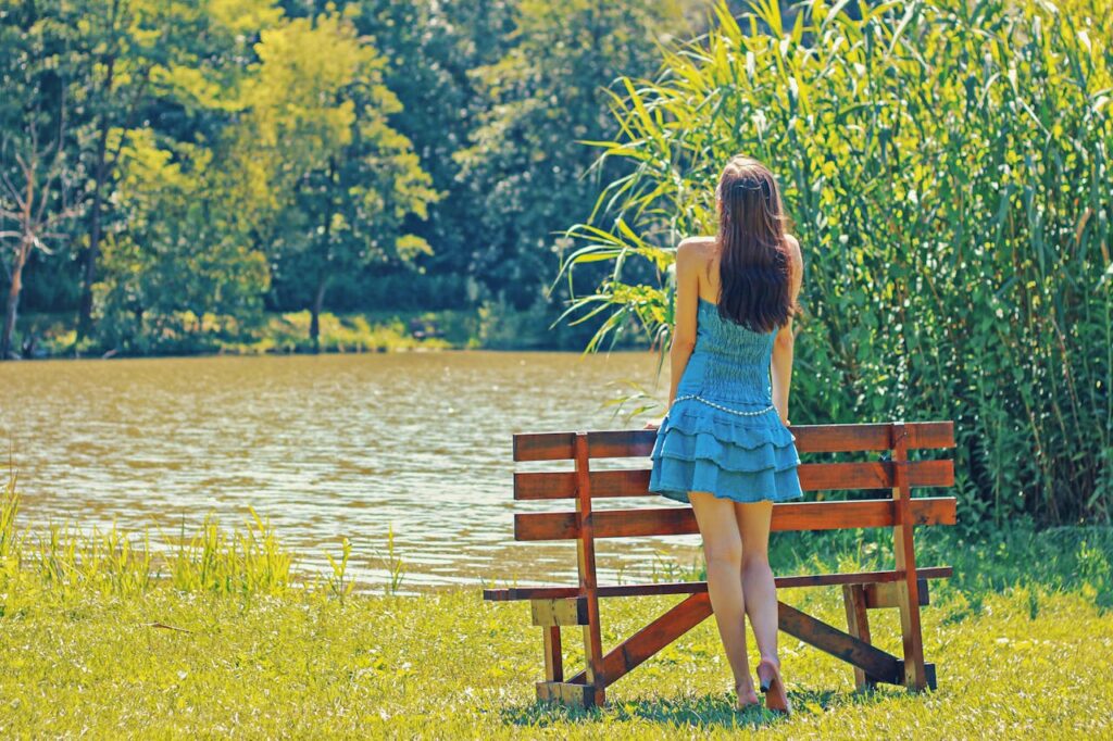 Woman enjoying a peaceful moment by a lake, embracing nature in summer.